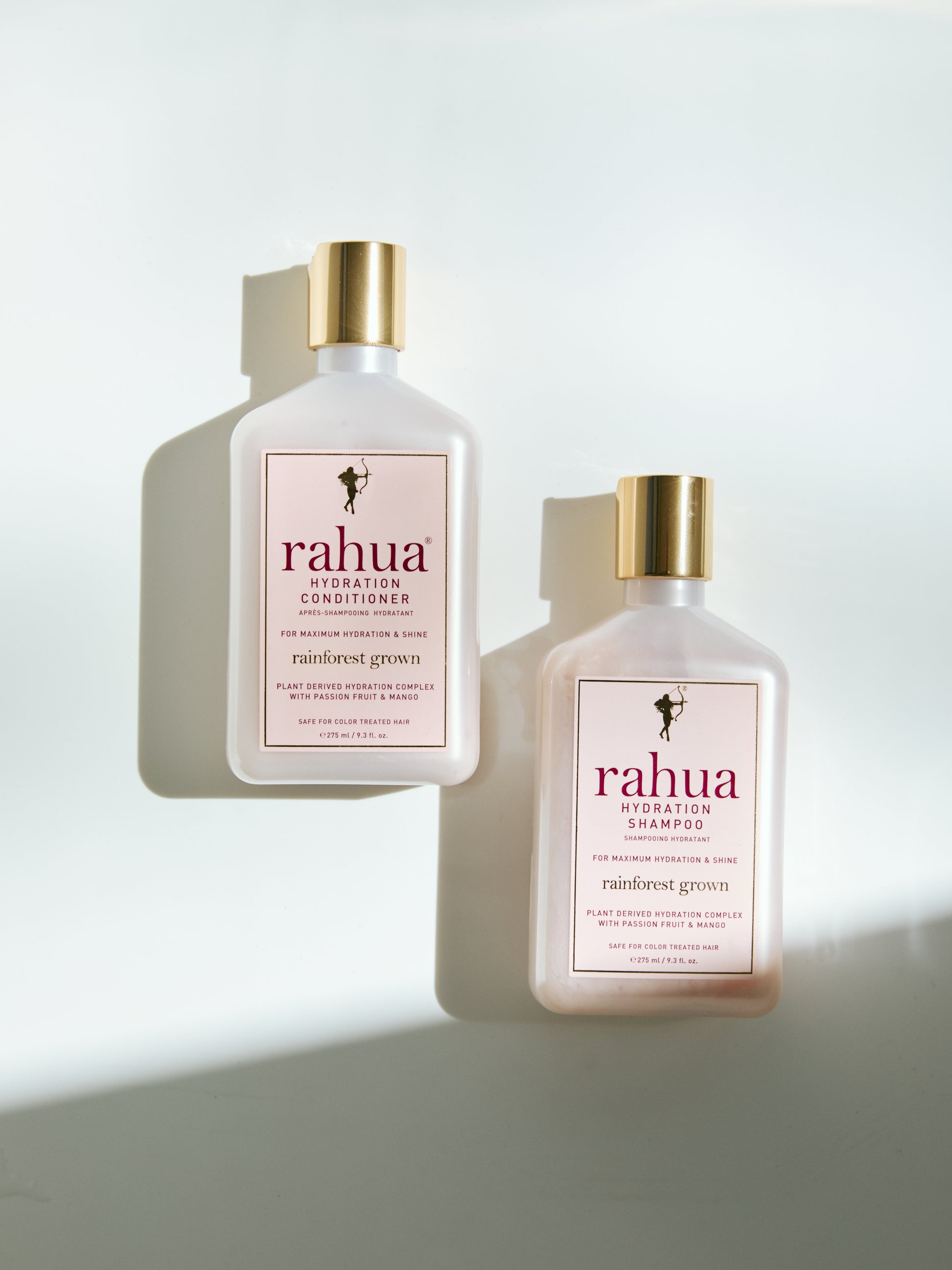 two bottles of rahua hydration conditioner and shampoo pink plastic bottles with gold caps set on a plain white background|variant:93-oz
