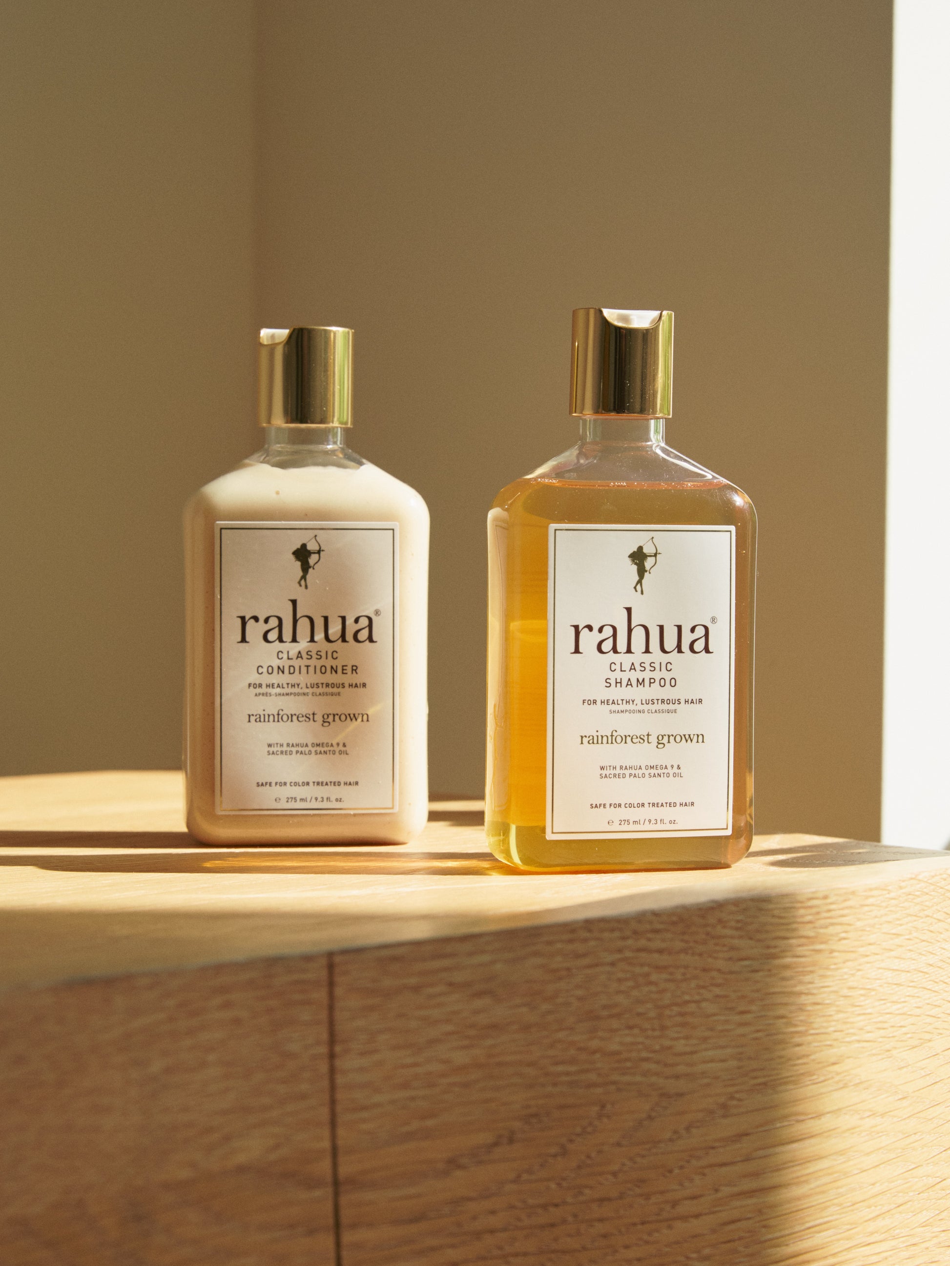 two bottles of rahua classic shampoo and classic conditioner on top of a wooden table on a plain beige background|variant:074-oz