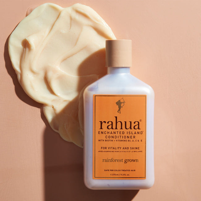 bottle of rahua enchanted island conditioner on a beige orange background with a spread of conditioner under the bottle to show product texture|variant:93-oz