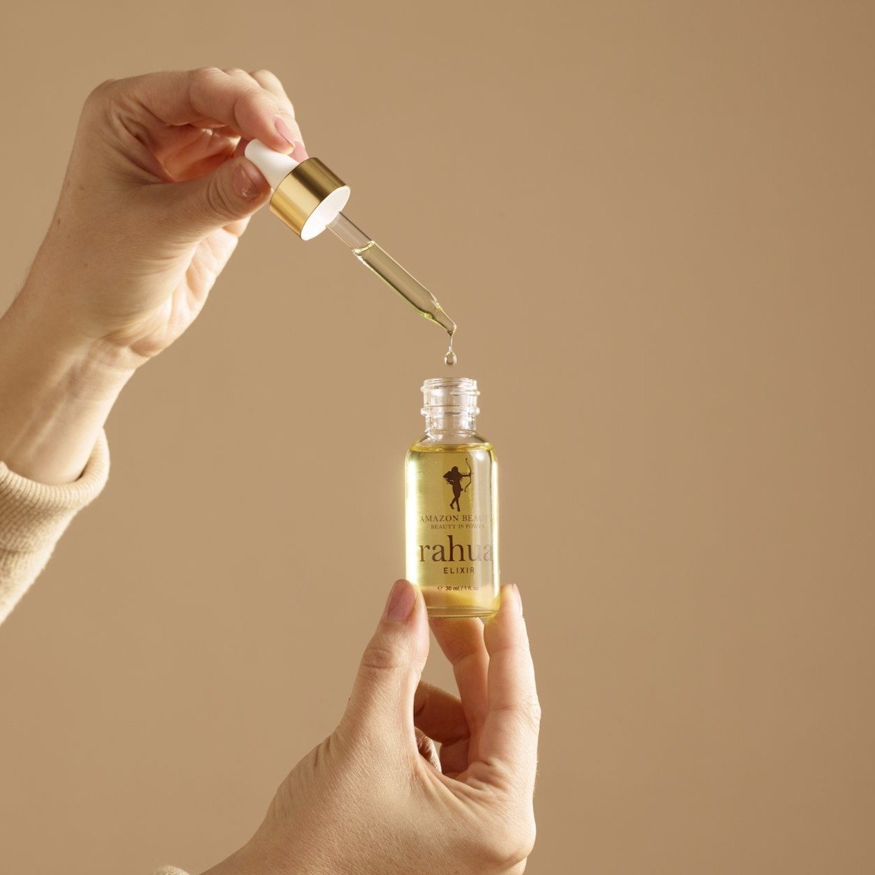 bottle of golden liquid in a glass bottle rahua elixir oil made of 100% rahua oil open bottle with model dropping in a drop of elixir|variant:1-oz