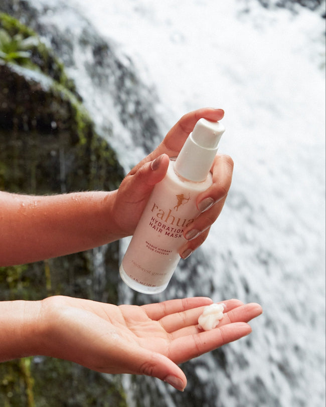 model dispensing product onto their hand glass bottle of rahua hydration hair mask with a background of a waterfall|variant:4-oz